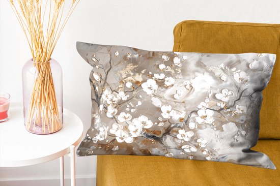 Coussin avec des branches de fleurs blanches et dorées sur un canapé jaune près d'une table d'appoint.