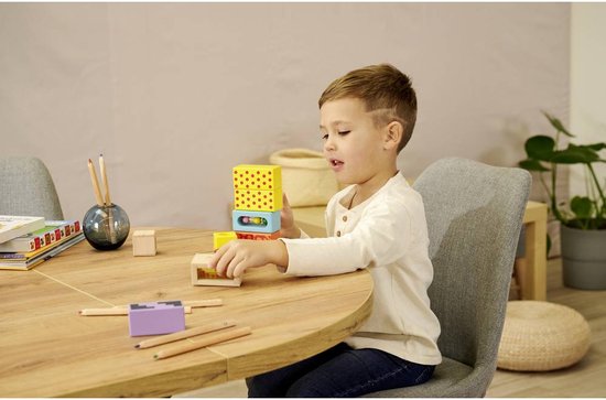 Een jongetje met bruine haren, zittend aan een tafel, speelt met houten blokken.