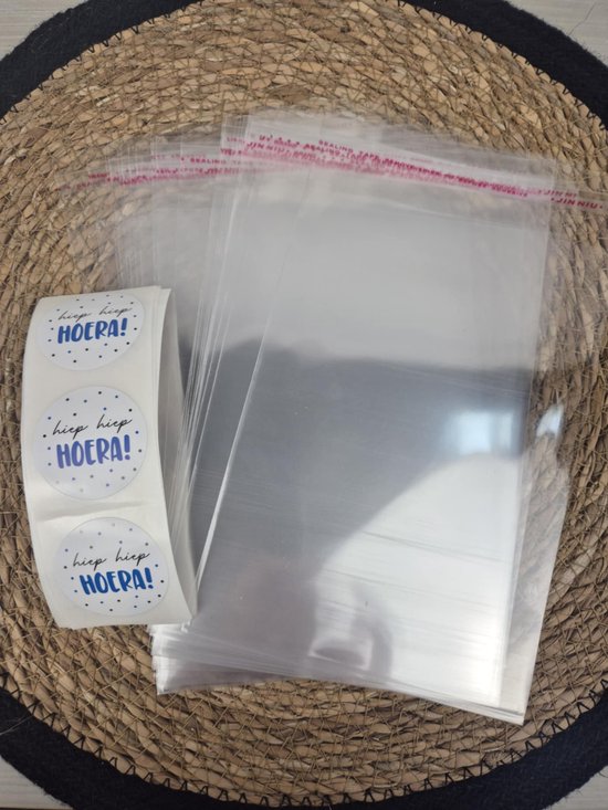 Transparante celofaan zakjes met rode plakrand, met een rol witte stickers met blauwe 'hiep hiep HOERA!' tekst en blauwe stipjes.