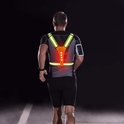 Man met rug naar voren, draagt een geel reflecterend hardloopvest met Y-banden en rode LED-verlichting op een donkere weg.