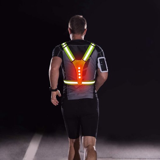 Man met rug naar voren, draagt een geel reflecterend hardloopvest met Y-banden en rode LED-verlichting op een donkere weg.