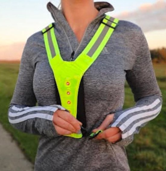 Vrouw draagt een geel reflecterend hardloopvest met Y-banden en LED-verlichting, terwijl ze het vest vastmaakt.