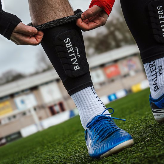 Voetballer trekt zwarte Vynix Ballers scheenbeschermers aan over witte sokken.
