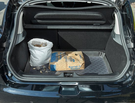 Tapis de coffre noir à motif losanges placé dans un coffre ouvert avec un sac de ciment et des débris.