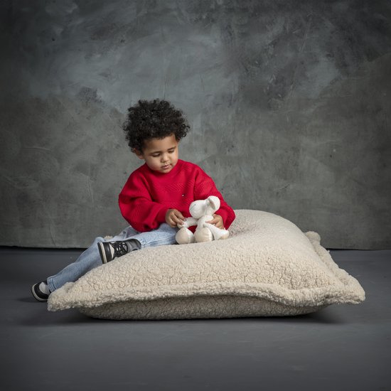 Jongetje met een rode trui en spijkerbroek zit op een crèmekleurig teddy zitkussen.