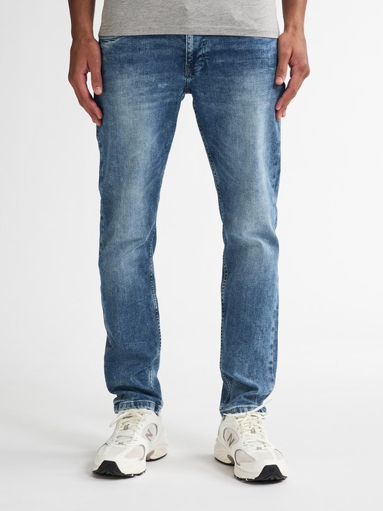 Man met een grijze T-shirt en blauwe jeans. De jeans is recht gesneden met een lichte wassing.