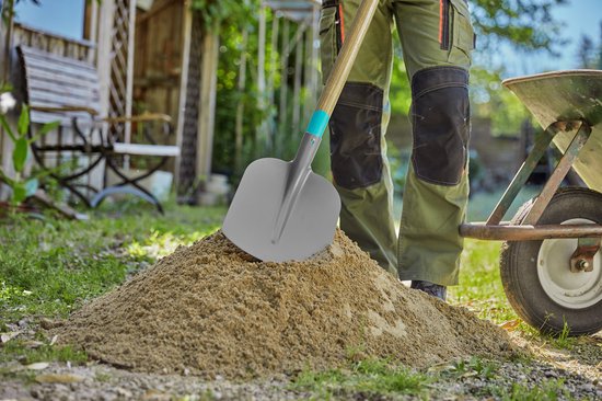 Een tuinman met een grijze schop met een turquoise accent, scheppend in een hoop zand, met een kruiwagen ernaast.