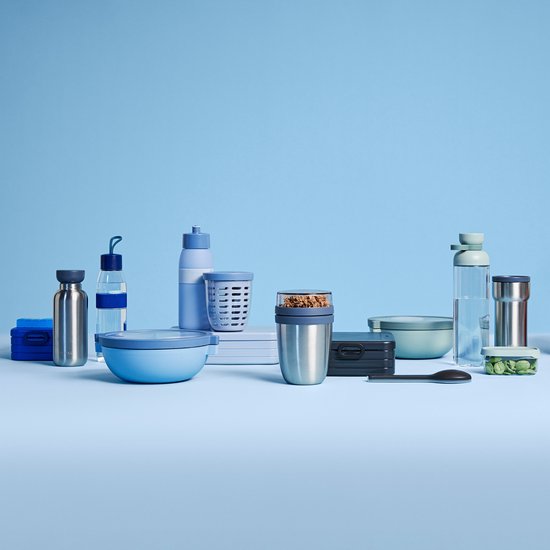 Pot à lunch en acier inoxydable avec couvercle transparent sur fond bleu, à côté d'autres produits Mepal.