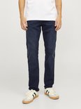 Donkerblauwe jeans gedragen door een man in een wit T-shirt en witte sneakers met groene en rode strepen.