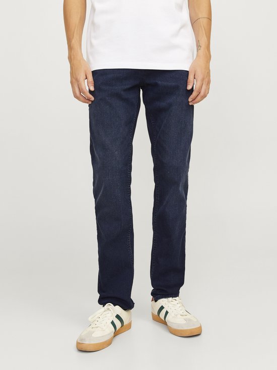 Donkerblauwe jeans gedragen door een man in een wit T-shirt en witte sneakers met groene en rode strepen.