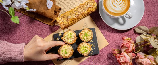 Hand die vier ronde gebakjes met hagelslag oppakt, naast een rol met amandelen en koffie.