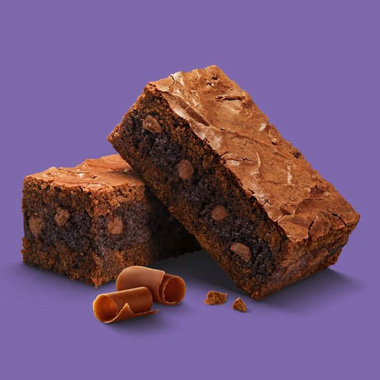 Twee Milka chocolade brownies met cacaokruimels en gesmolten stukjes chocolade, op een paarse achtergrond.