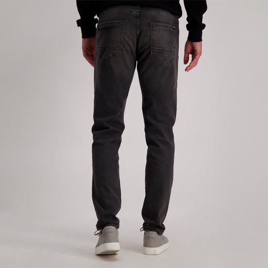 Man met donkere spijkerbroek en grijze sneakers, van achteren gezien.