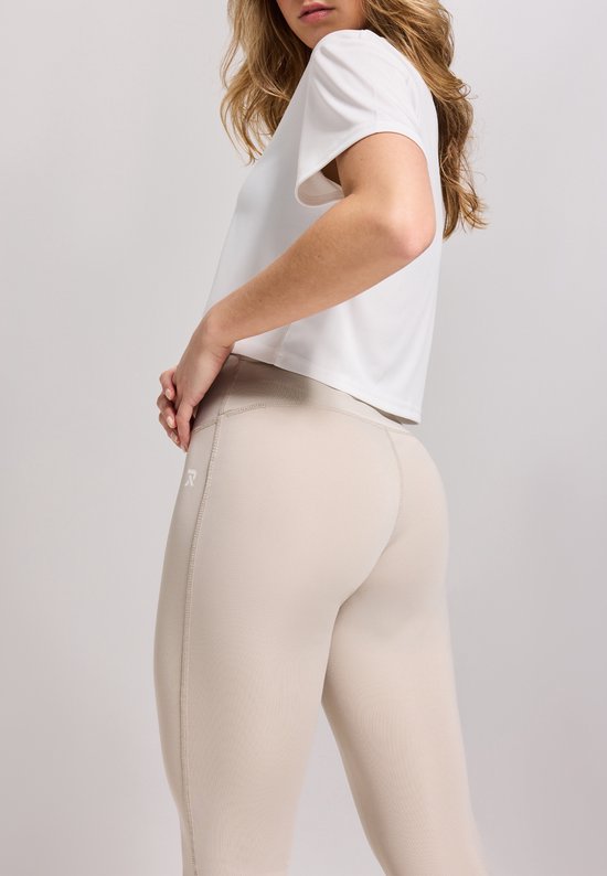 Vrouw in een beige legging met logo 'R' en witte crop top.
