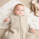 Baby in een zandkleurige, gevoerde slaapzak met rits. Ligt op een laken met takjesprint.