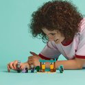 Een jongen met krullend haar kijkt geconcentreerd naar LEGO Minecraft poppetjes en een kleine woestijnbasis op een blauwe achtergrond.