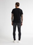 Man met tatoeages, achterkant, draagt een strakke zwarte spijkerbroek en zwarte T-shirt.