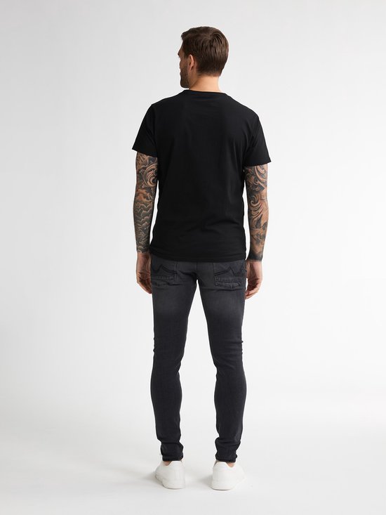 Man met tatoeages, achterkant, draagt een strakke zwarte spijkerbroek en zwarte T-shirt.