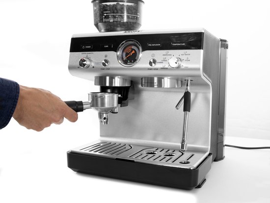 Zilverkleurige Krups espressomachine met ingebouwde grinder, een hand die een portafilter vasthoudt.