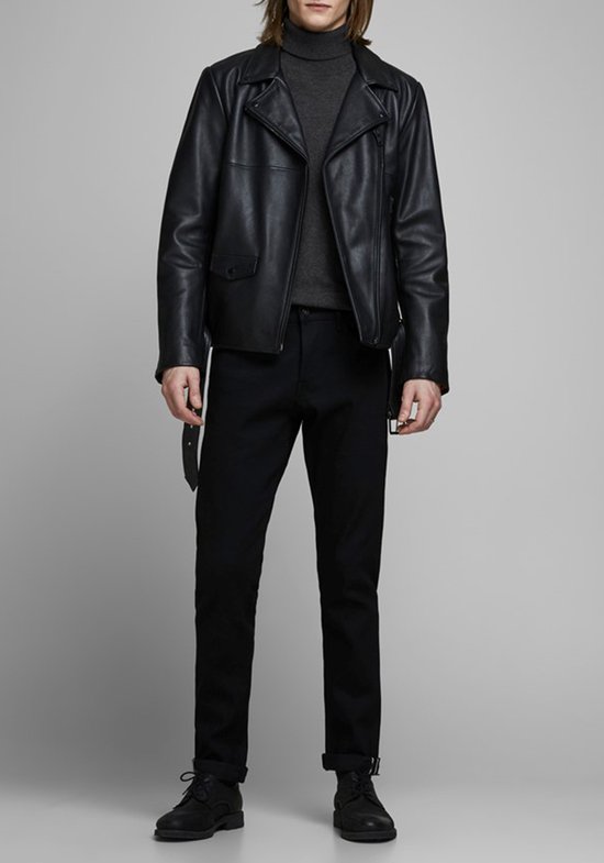 Man in een donkergrijs coltrui en zwarte broek, met een leren bikerjack open.