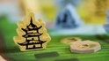 Geel houten speelfiguur in de vorm van een Chinese pagode op een bordspel met groene heuvels.