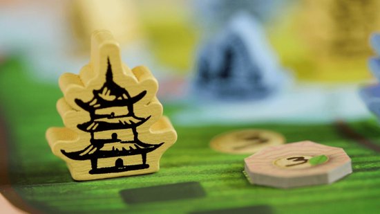 Geel houten speelfiguur in de vorm van een Chinese pagode op een bordspel met groene heuvels.