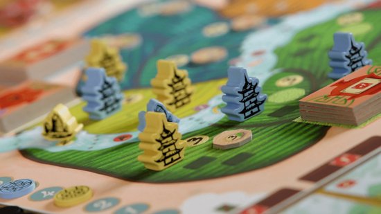 Bordspel met gele en blauwe pagode-achtige speelfiguren op een groene ondergrond met een rivier.