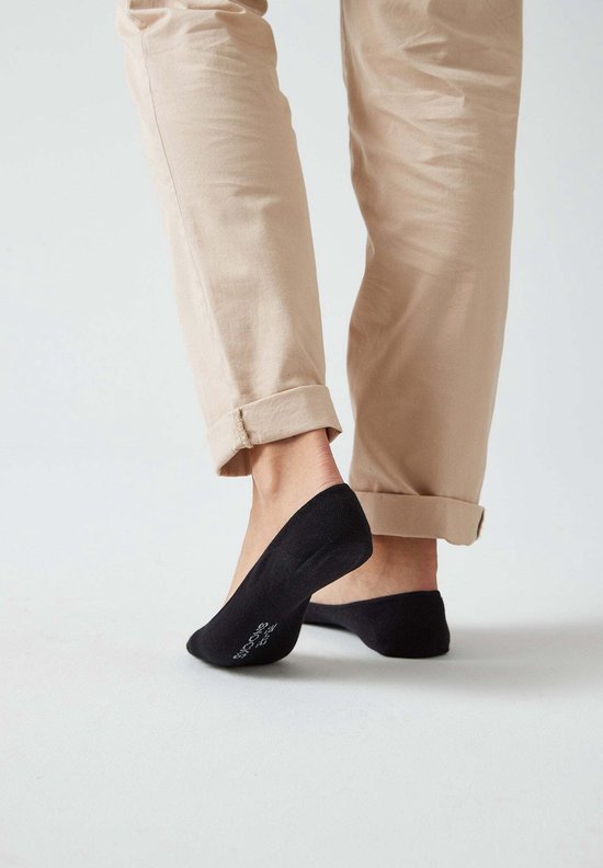 Zwarte onzichtbare sokken op de voeten van een vrouw met beige broek.