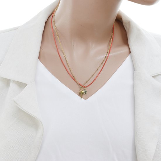 Dubbele gouden ketting met koraalrode kraaltjes, munthanger en kruishanger gedragen met een wit jasje.