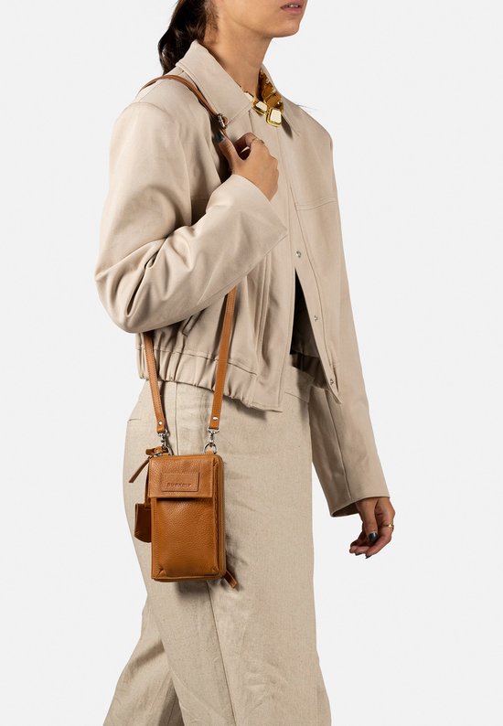 Model met cognac telefoonportemonnee gedragen als crossbody tas, met beige jas en broek.