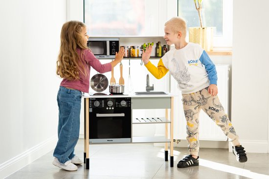 Jongen en meisje spelen bij een witte houten speelkeuken.