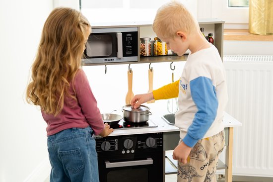 Kinderen spelen met een speelkeuken. Jongen kijkt in potje, meisje bedient fornuis.