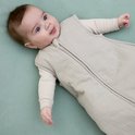 Baby in een lichtgrijze Meyco slaapzak liggend op een groen ondergrond.