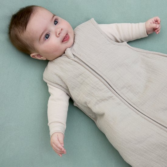 Baby in een lichtgrijze Meyco slaapzak liggend op een groen ondergrond.