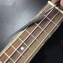 Een hand gebruikt een platte vijl om op de metalen frets van een houten gitaarhals te werken.