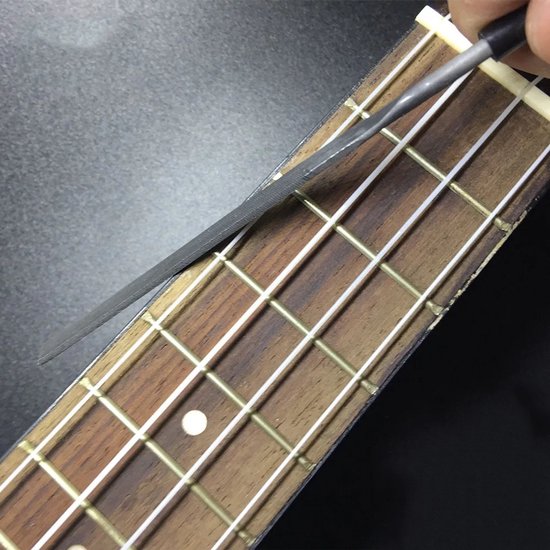 Een hand gebruikt een platte vijl om op de metalen frets van een houten gitaarhals te werken.