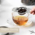 Hand houdt zilverkleurige theezeef met losse theeblaadjes boven een glas met amberkleurige thee. "Elegant filtering" tekst.