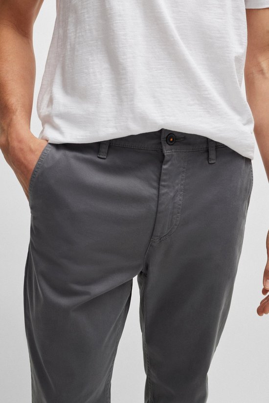 Sluiting van de antracietkleurige chino met knoop, oranje detail en rits. De broek is van het merk BOSS.