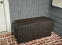 Bruine opbergbox met gesloten deksel, naast een deur met grijze gevelbekleding en bakstenen.
