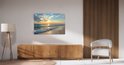 Canvas schilderij met zonsondergang aan zee, hangend boven een houten kast met een witte stoel.