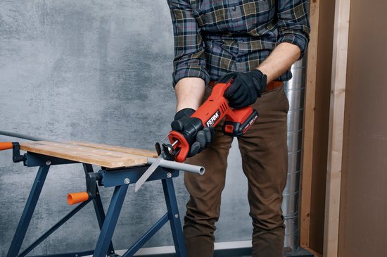 Man met handschoenen zaagt met een rode en zwarte reciprozaag een grijze buis op een werktafel.