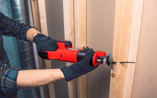 Man met handschoenen zaagt met een rode en zwarte reciprozaag door een houten muur.