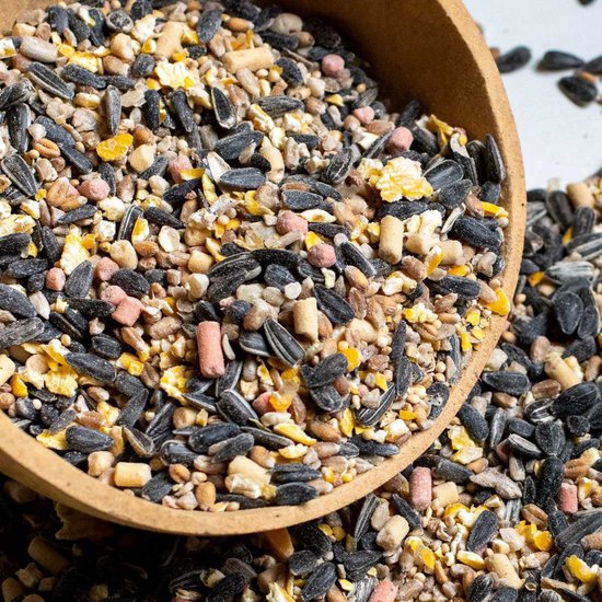 Vogelvoer in een houten schaal, met zaden, pitten en kleine roze en gele pellets.