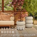 Twee crèmekleurige, gestapelde bloempotten met een matte afwerking. Een rode Japanse esdoorn staat in de linker pot. Rechts een olijfgroene struik. Een persoon ligt op een bankje.