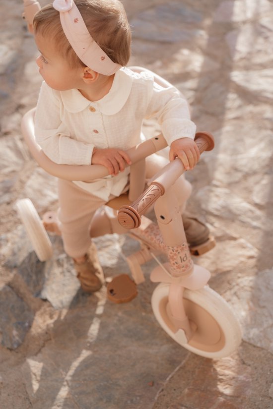 Baby in roze outfit op een roze driewieler met bloemenprint.