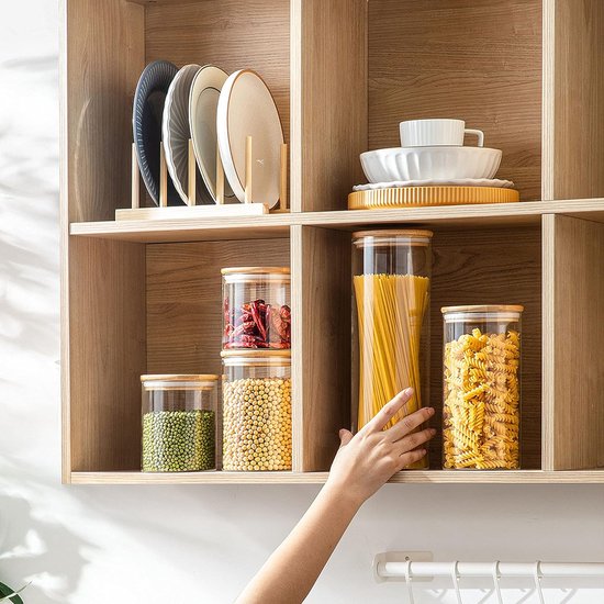 Glazen voorraadpotten gevuld met pasta en andere voedingsmiddelen, op een open kast. Een hand pakt een pot.