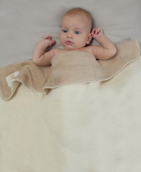 Baby liggend op een beige deken, deken heeft een lichte beige afwerking en een zachte textuur.
