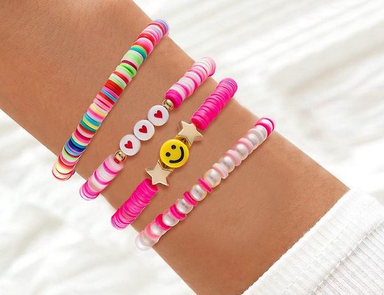 Een pols met diverse polymeerklei armbanden in roze, wit, met hartjes, parels en een smileygezicht.