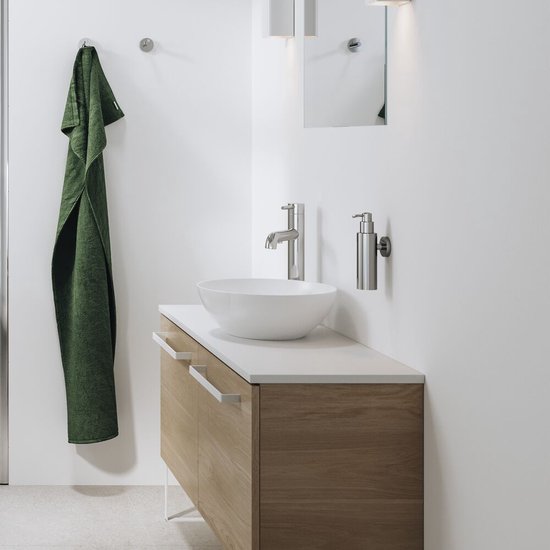 Badkamer met houten kastje, witte wastafel, RVS kraan en RVS zeepdispenser.
