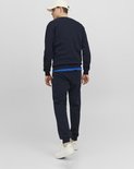 Man, achterkant, in donkerblauwe sweater en joggingbroek, met een beige pet en witte sneakers.